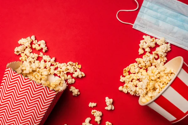 Vista superior de cubos con palomitas de maíz y máscara médica sobre fondo rojo - foto de stock