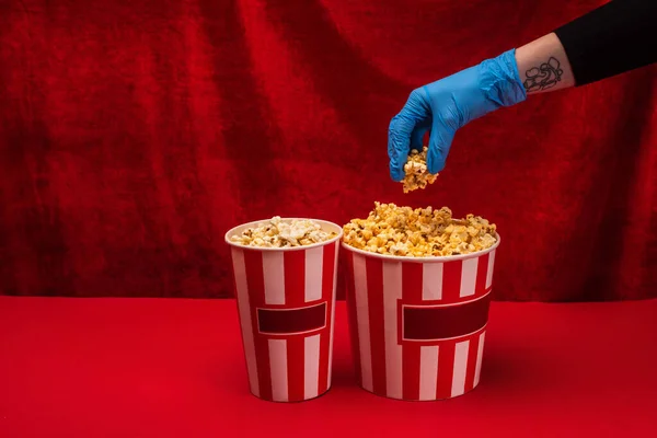 Ausgeschnittene Ansicht einer Frau im Latex-Handschuh mit Popcorn auf roter Oberfläche und Velours im Hintergrund — Stockfoto