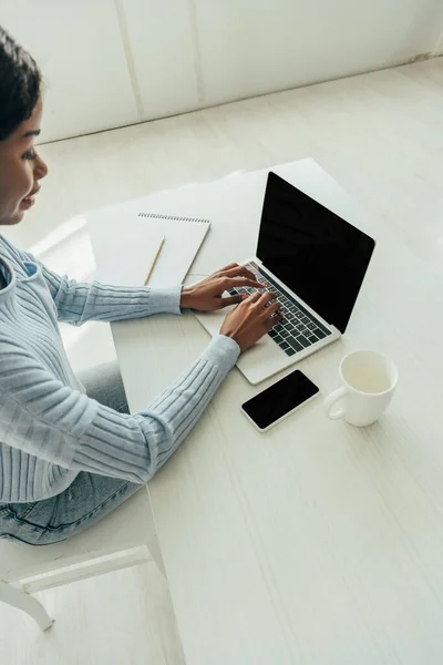 High angle view of african american freelancer using laptop with blank screen near smartphone and empty cup — Stock Photo