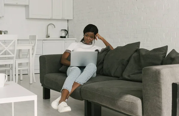 Concentrado Africano americano freelancer trabalhando no laptop no sofá na cozinha — Fotografia de Stock