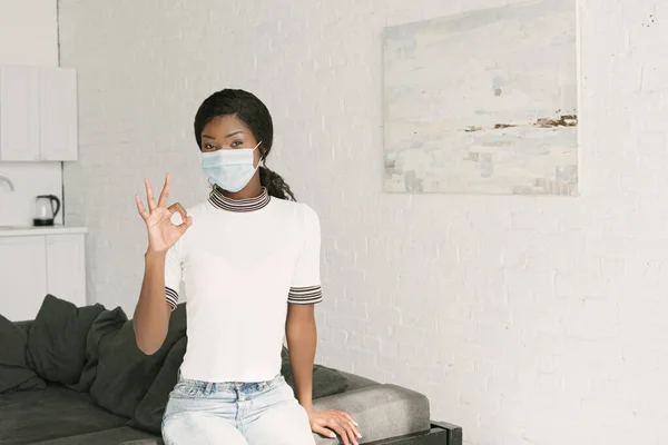 Menina americana africana em máscara médica mostrando gesto ok enquanto olha para a câmera — Fotografia de Stock