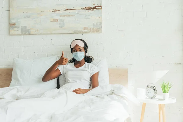 Afrikanerin in medizinischer Maske zeigt Daumen nach oben, während sie in die Kamera schaut — Stockfoto