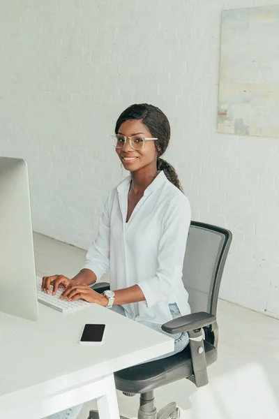 Happy african american freelancer typing on keyboard while smiling at camera — Stock Photo