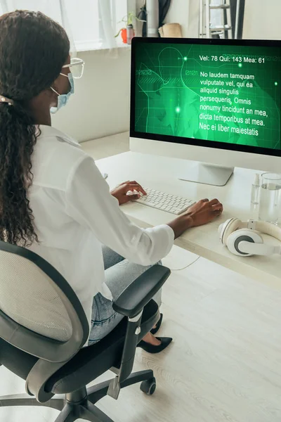 Young african american freelancer in medical mask looking at computer monitor with medical website on screen — Stock Photo