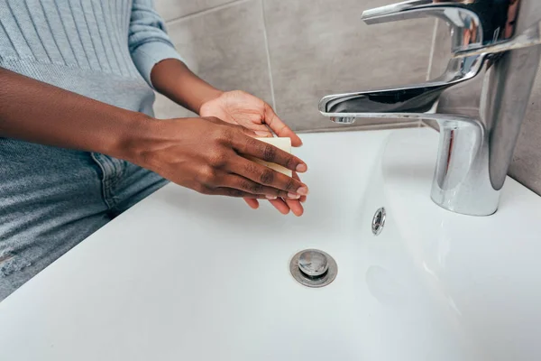 Vista parcial de mujer afroamericana sosteniendo jabón cerca del lavabo en el baño - foto de stock
