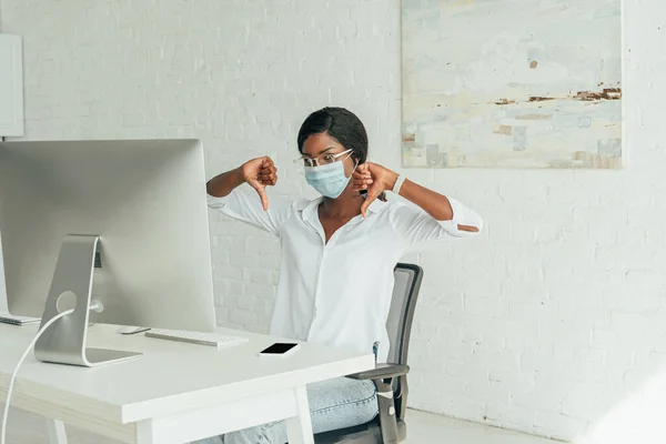 Dispiaciuto afro-americano freelance mostrando pollici verso il basso mentre seduto vicino al monitor del computer a casa — Foto stock