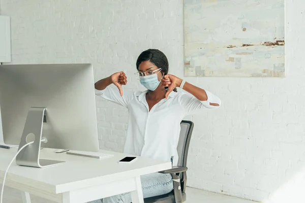 Displeased african american freelancer showing thumbs down while sitting near computer monitor at home — Stock Photo