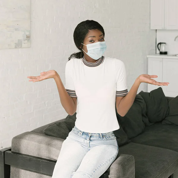 Femme afro-américaine confus dans le masque médical montrant geste haussant les épaules tout en regardant la caméra — Photo de stock