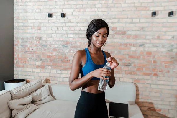 African american sportswoman closing sports bottle with lid in living room — Stock Photo