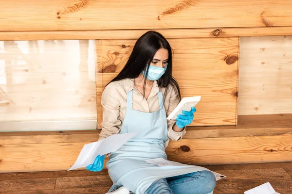 Cafe owner in medical mask holding documents and looking at calculator on floor — Stock Photo
