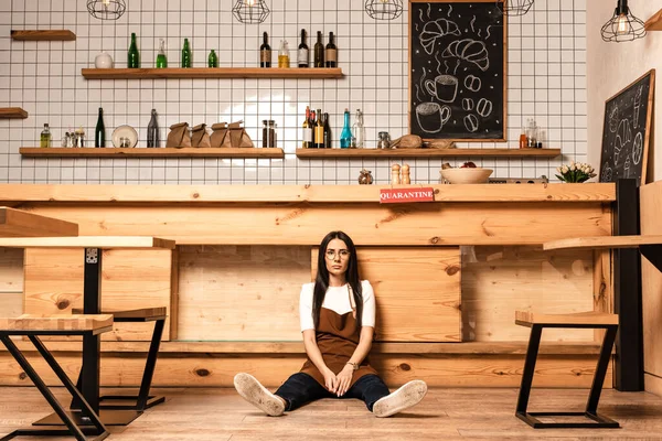 Propietario del café mirando a la cámara y sentado en el piso cerca de la mesa - foto de stock