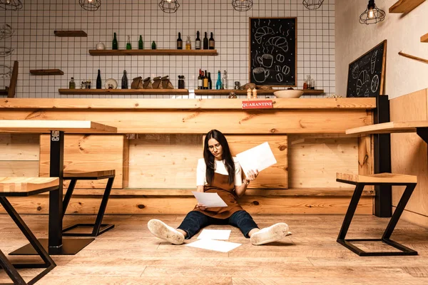 Concentrated cafe owner looking at document and sitting near table on floor — Stock Photo
