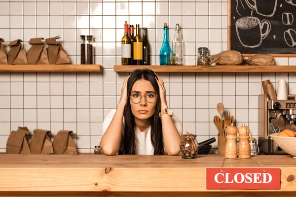 Verärgerter Café-Besitzer blickt auf Kamera am Tisch mit Pfeffer- und Salzmühlen und Karte mit geschlossener Aufschrift — Stockfoto