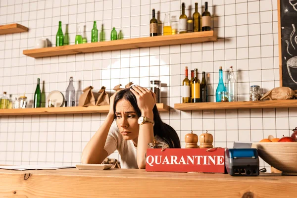 Upset cafe owner at table with calculator, card with quarantine lettering, payment terminal and bowl with fruits — Stock Photo