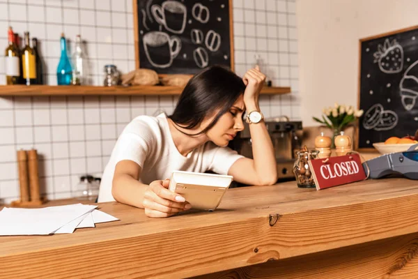 Aufgebrachter Café-Besitzer mit geschlossenen Augen, Taschenrechner in der Hand und auf Tisch gestützt mit Papieren und Karte mit geschlossener Aufschrift — Stockfoto