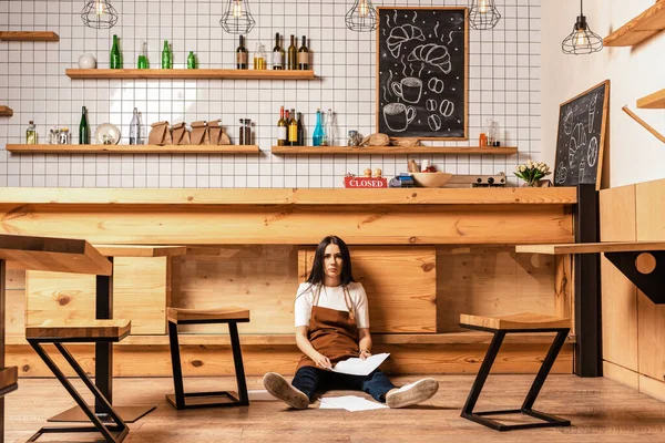 Cafébesitzer mit Dokumenten blickt in die Kamera neben Tisch und Stühlen auf dem Boden — Stockfoto