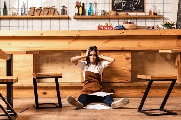 Stressed cafe owner with closed eyes and papers near table and chairs on floor — Stock Photo