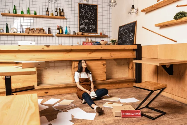 Cafe owner with calculator sitting near table, papers and card with quarantine lettering on floor — Stock Photo