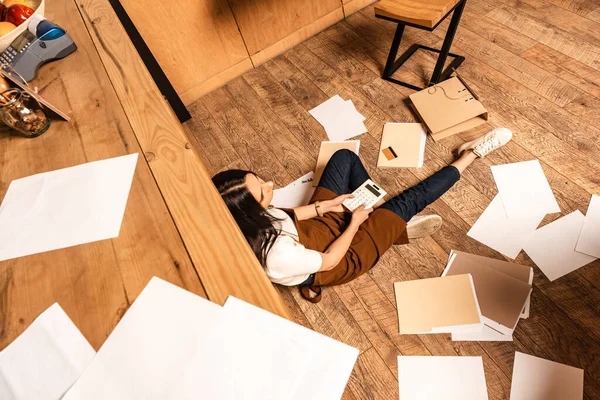 Ansicht des Cafébesitzers mit Taschenrechner in der Nähe des Tisches, Papieren, Kreditkarte und Ordnern auf dem Fußboden — Stockfoto