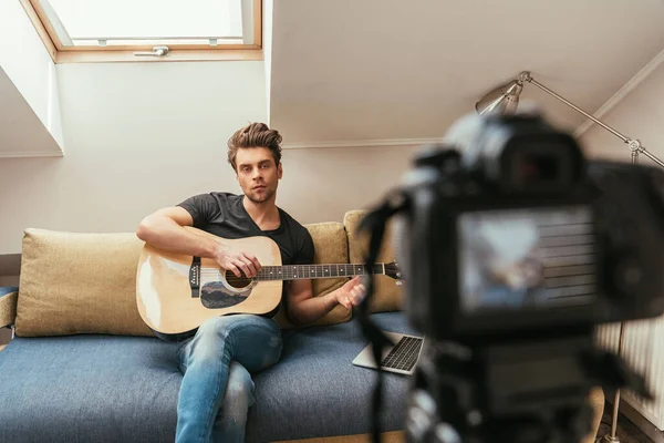 Foyer sélectif de vlogger réfléchi jouer de la guitare tout en regardant appareil photo numérique — Photo de stock