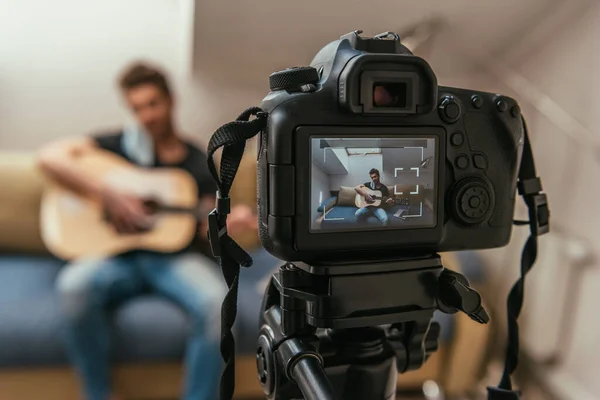 Selective focus of young vlogger playing guitar while looking at digital camera — Stock Photo