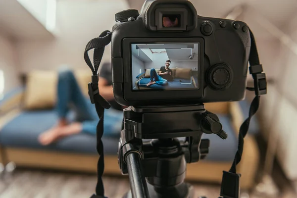 Selective focus of digital camera with young vlogger knitting on sofa at home — Stock Photo