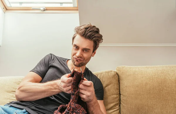 Mécontent homme regardant la caméra tout en tricotant sur le canapé à la maison — Photo de stock