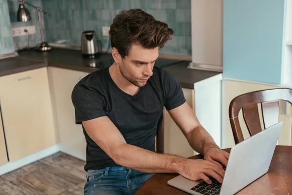 Hombre concentrado en camiseta negra trabajando en el ordenador portátil en casa - foto de stock