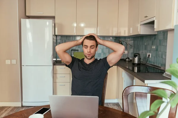 Homme épuisé touchant la tête tout en regardant le moniteur d'ordinateur portable dans la cuisine — Photo de stock