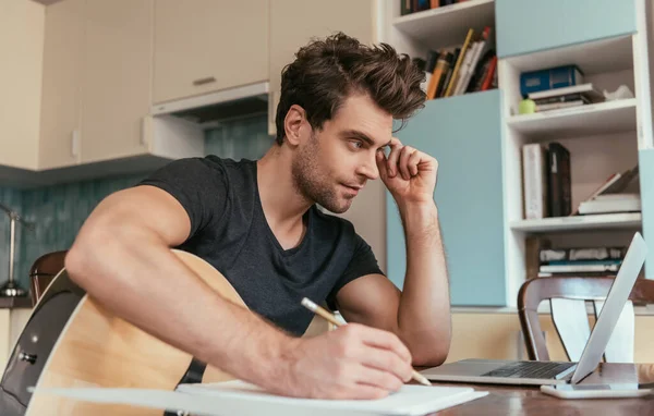 Jeune homme attentif avec des notes d'écriture de guitare tout en regardant ordinateur portable — Stock Photo