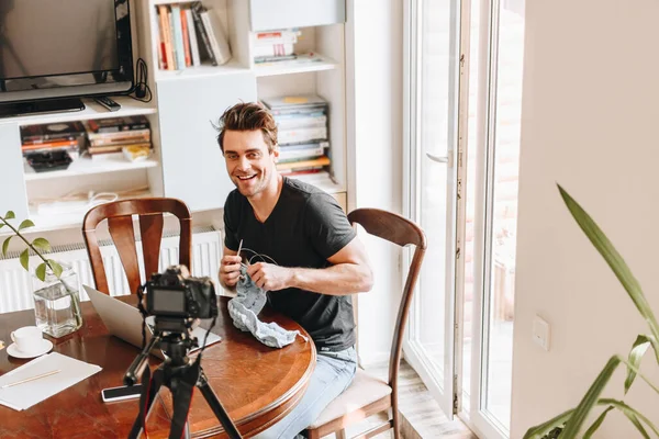 Vista de ángulo alto del vlogger sonriente tejiendo mientras mira la cámara digital en el trípode - foto de stock