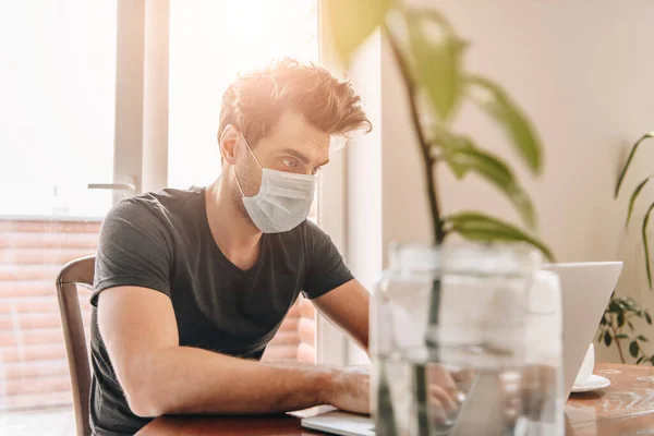 Selective focus of young, concentrated man in medical mask working on laptop at home — Stock Photo
