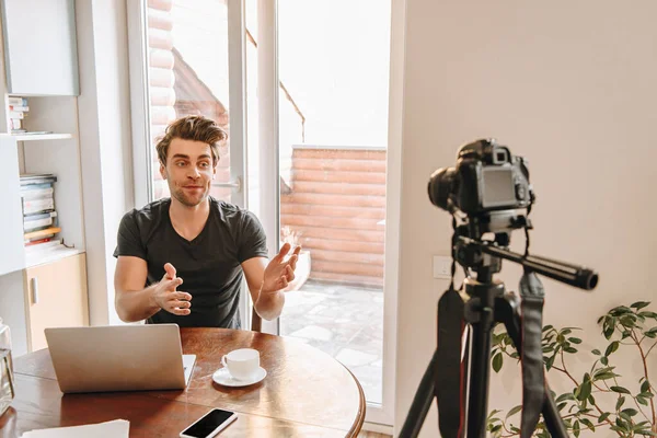 Junger Videoblogger spricht und gestikuliert, während er die Digitalkamera auf Stativ betrachtet — Stockfoto