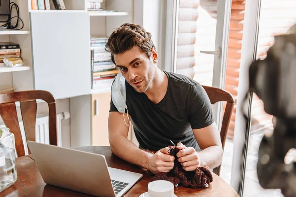 Young vlogger with medical mask on ear knitting while looking at digital camera — Stock Photo