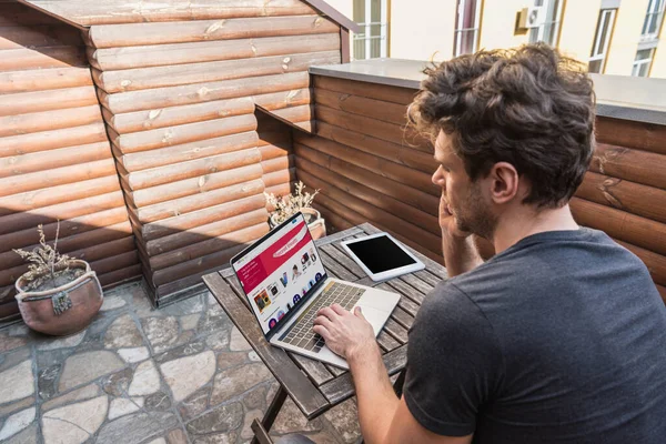 KYIV, UKRAINE - 13 AVRIL 2019 : jeune homme utilisant un ordinateur portable avec le site Web Ebay assis sur le balcon — Photo de stock