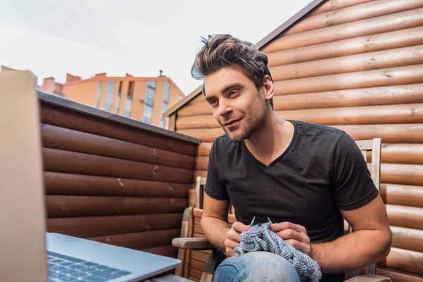 Attentive young man looking at laptop while knitting on balcony — Stock Photo