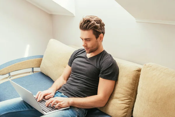 Konzentrierter Mann benutzt Laptop, während er zu Hause auf dem Sofa sitzt — Stockfoto