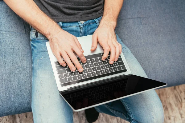 Vue recadrée de l'homme en jeans denim tapant sur ordinateur portable avec écran blanc, vue du dessus — Photo de stock