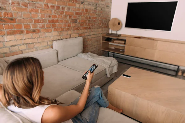 Menina segurando controlador remoto e assistir tv com tela em branco durante o auto-isolamento, foco seletivo — Fotografia de Stock