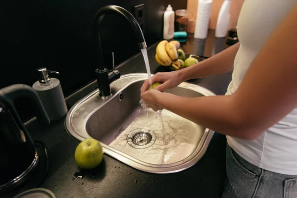 Vista ritagliata di donna che lava frutta nel lavandino sulla cucina durante la quarantena — Foto stock