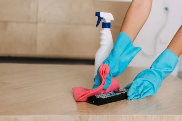 Cropped view of woman in rubber gloves cleaning remote controller with rag and antiseptic spray during quarantine — Stock Photo