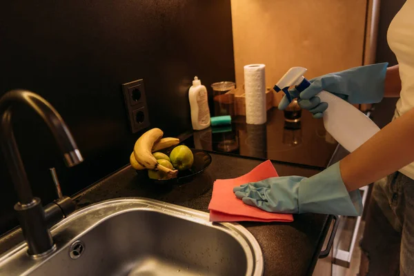 Vista recortada de la mujer en guantes de goma fregadero de limpieza con trapo y spray antiséptico durante la cuarentena - foto de stock