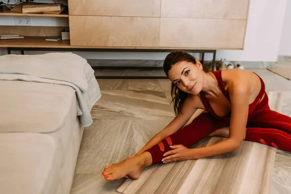 Красивая улыбающаяся девушка растягивается на коврике для йоги дома на карантине — стоковое фото