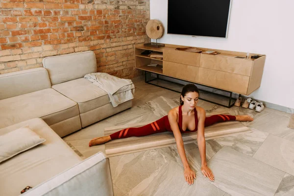 Спортивна дівчина сидить в шпагаті на йога килимок вдома під час самоізоляції — стокове фото
