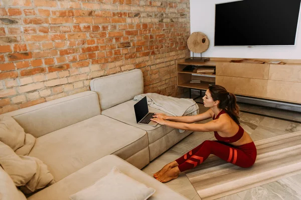 Привлекательные тренировки девушки online с ноутбуком на циновке yoga на дому на self isolation — стоковое фото