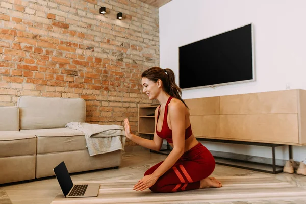 Treinamento menina feliz on-line com laptop no tapete de ioga em casa no auto isolamento — Fotografia de Stock