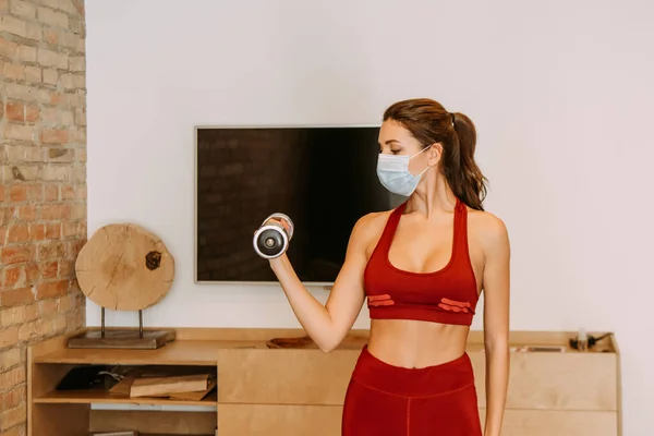 Femme attrayante dans la formation de masque médical avec haltère à la maison pendant l'isolement personnel — Photo de stock