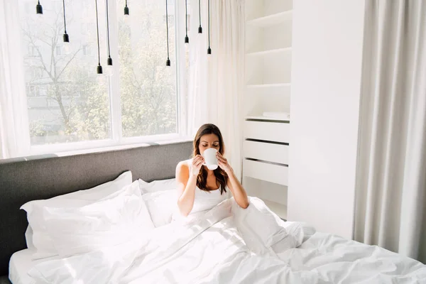 Привлекательная женщина пьет кофе в постели утром во время самоизоляции — стоковое фото
