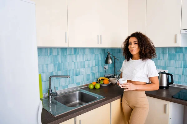 Cheerful african american girl holding cup near fresh fruits — Stock Photo