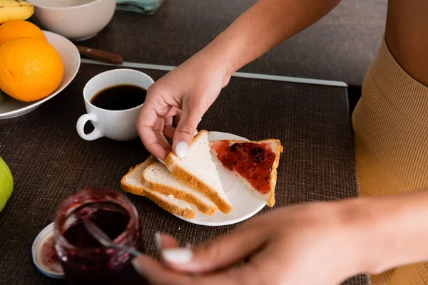 Cropped view of african american girl holding spoon and toast bread near ripe fruits on table — Stock Photo